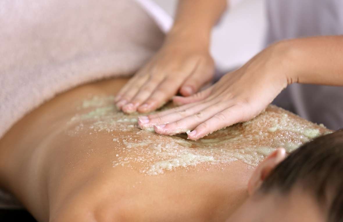 A person receiving a body scrub treatment with a granular product being applied to their back.