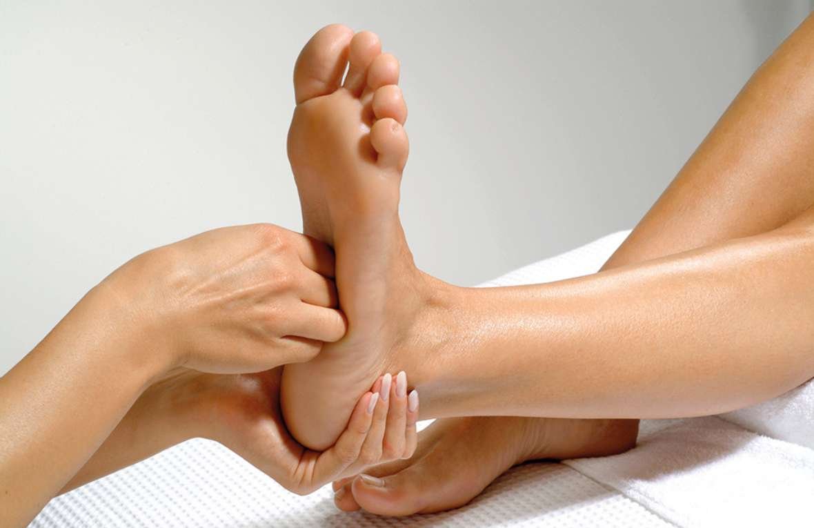 A person receiving a foot massage, with a therapist's hands working on their foot.